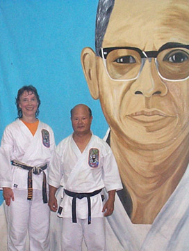 Sensei Cyndy Jones with Master Kichiro Shimabuku in front of picture of Isshinryu Founder Tatsuo Shimabuku